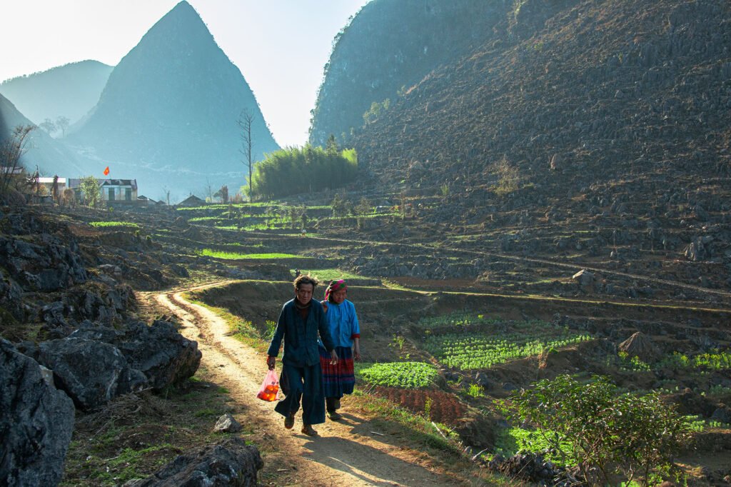 Two hikers walking on the Sky Path trail, which offers stunning views of the Ma Pi Leng mountain range in Ha Giang, Vietnam.
